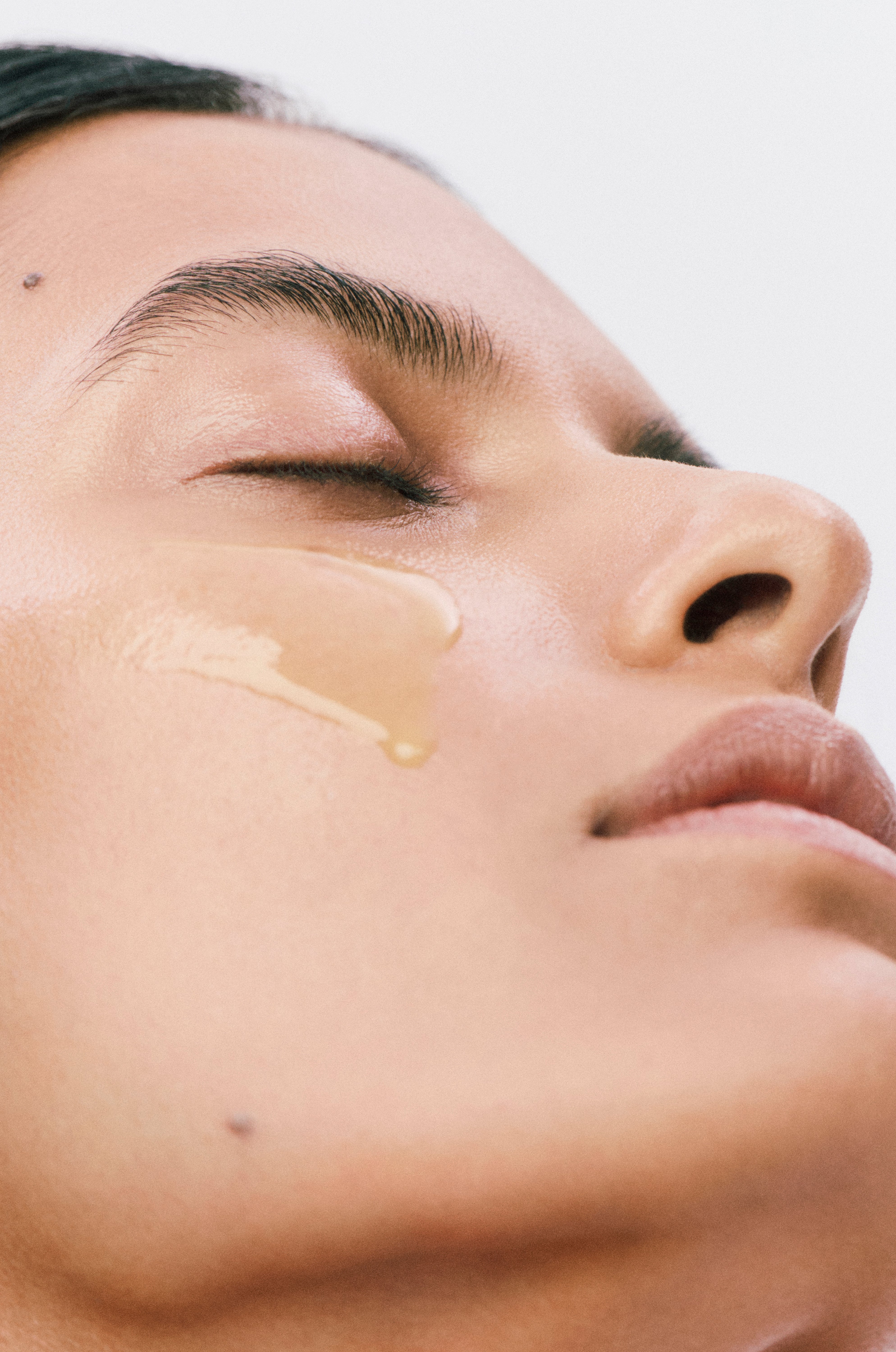 Close-up of a person applying a skincare product with a yellow hue to their face.