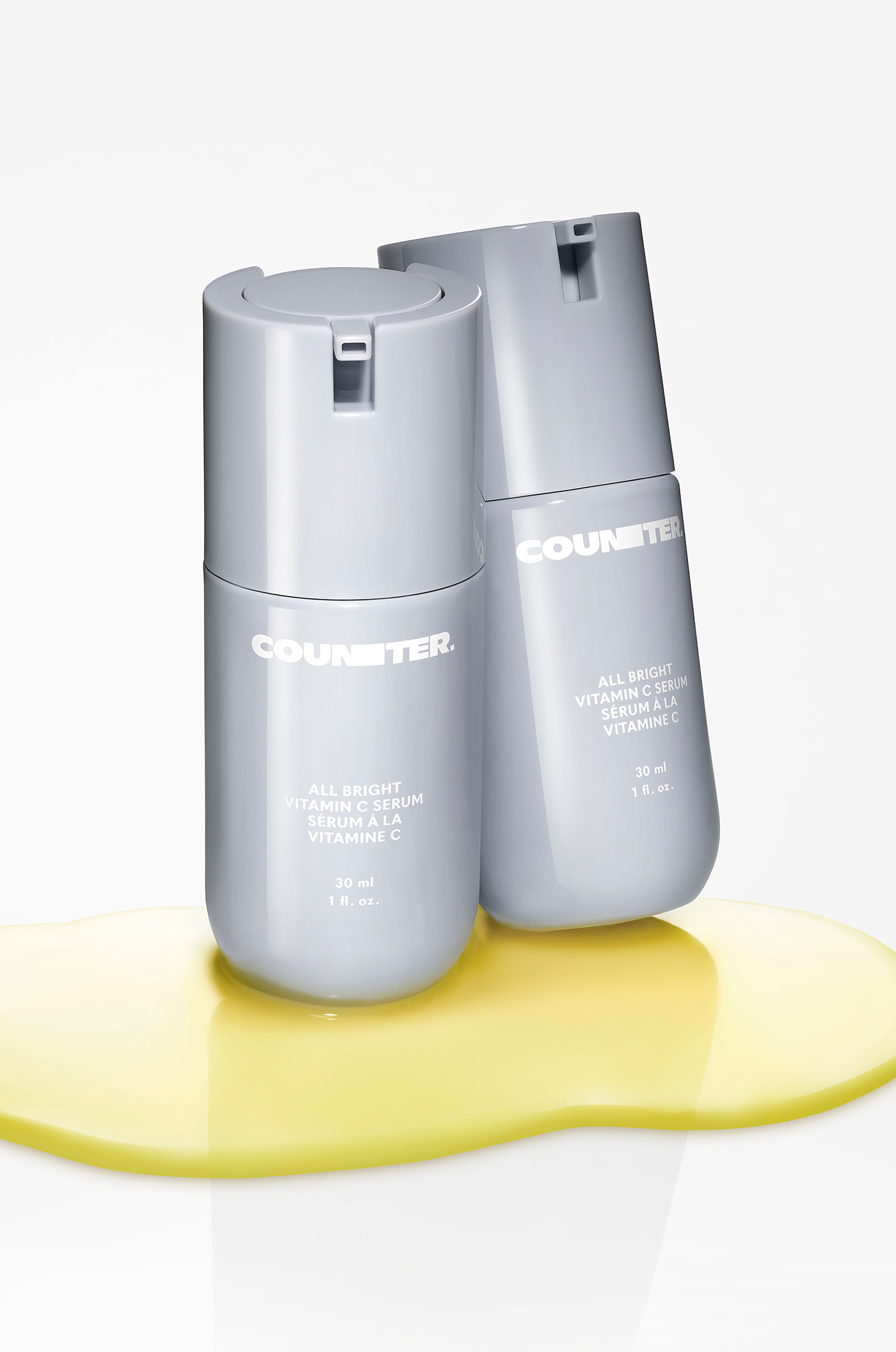 Two light grey skincare bottles with a yellow serum on a white background