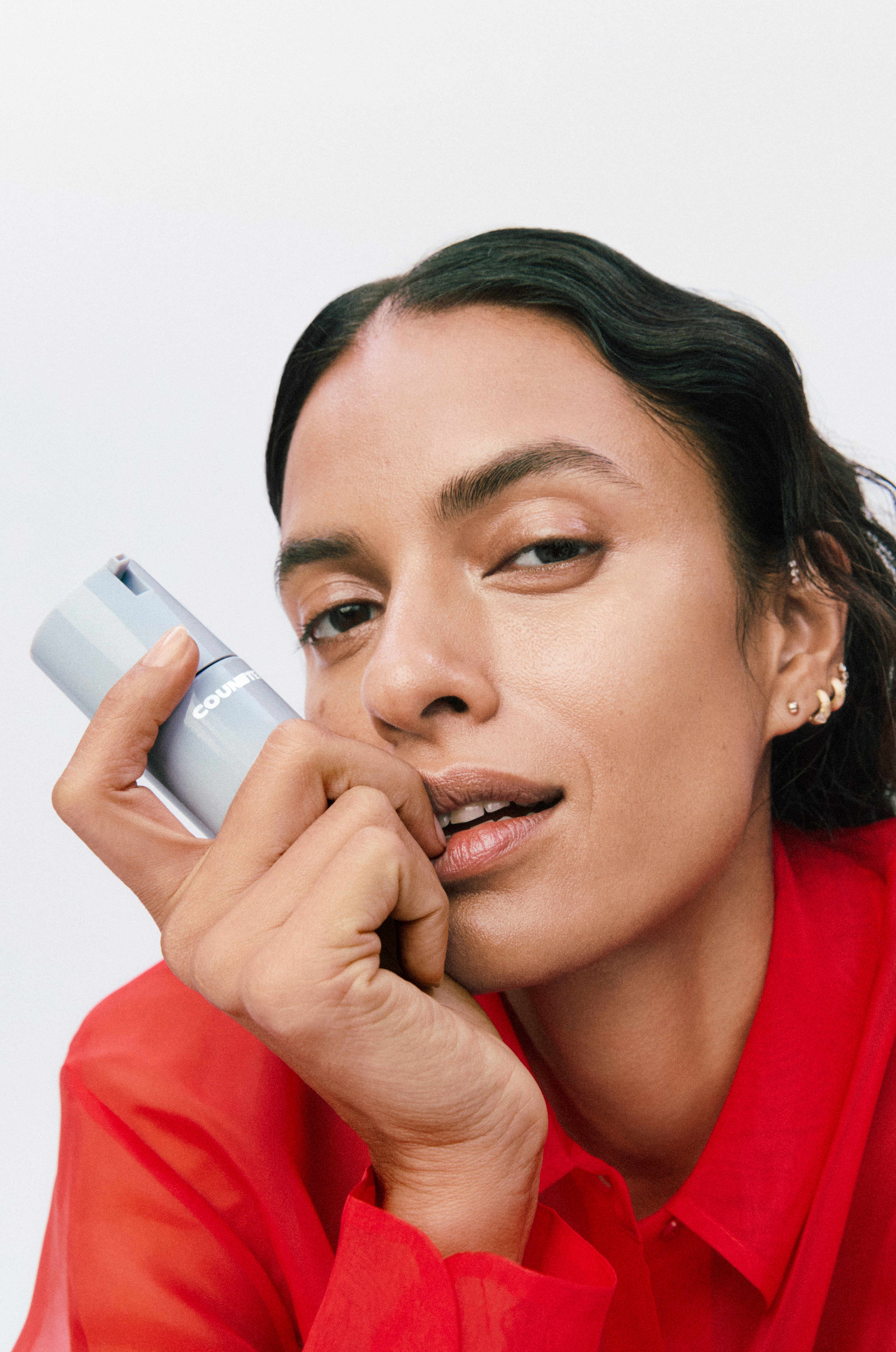 Woman holding a small light grey bottle of counter product against a white background