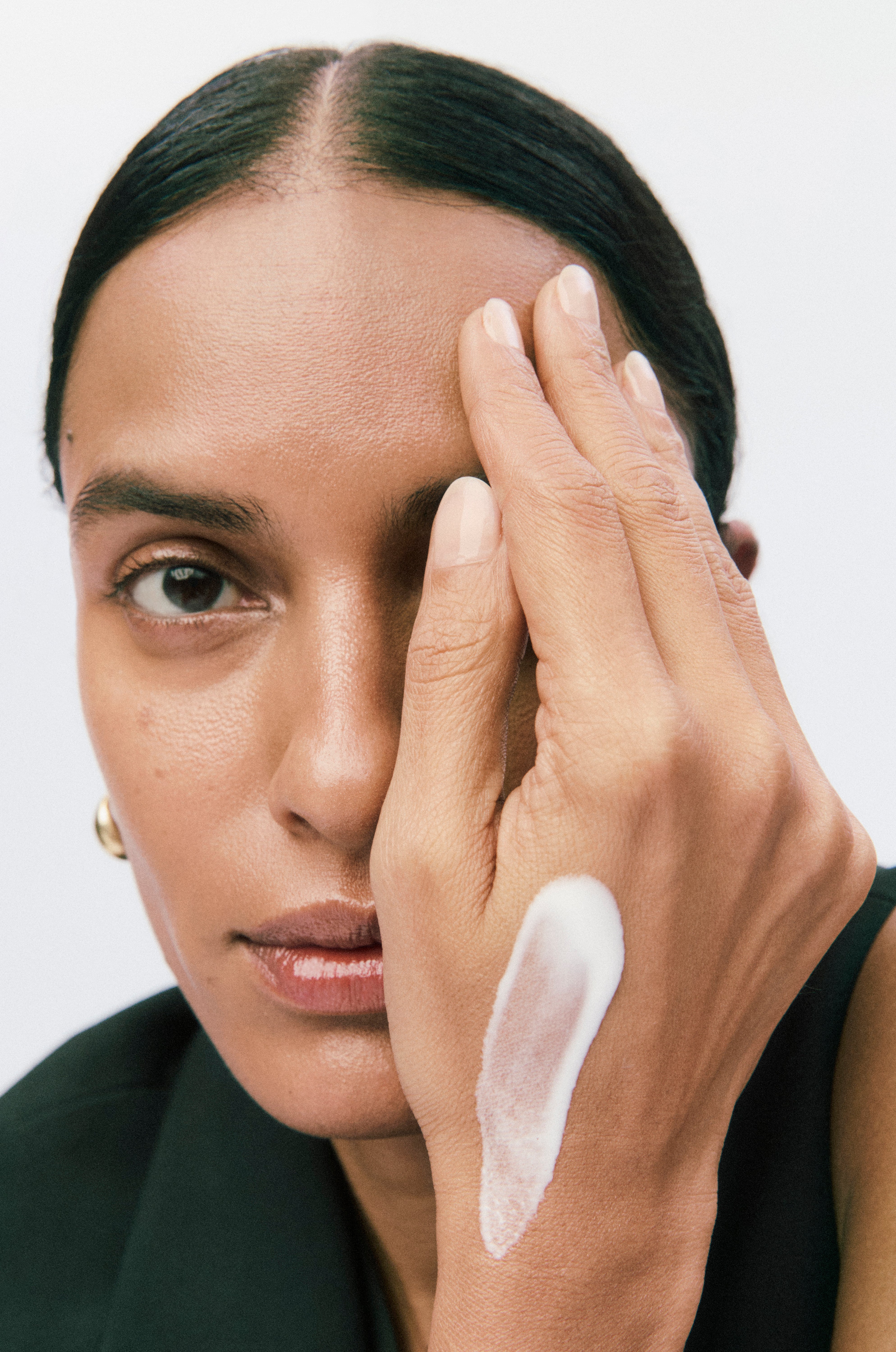 Displays a model covering half of her face with her hand. On her hand is a smear of white Counter product.
