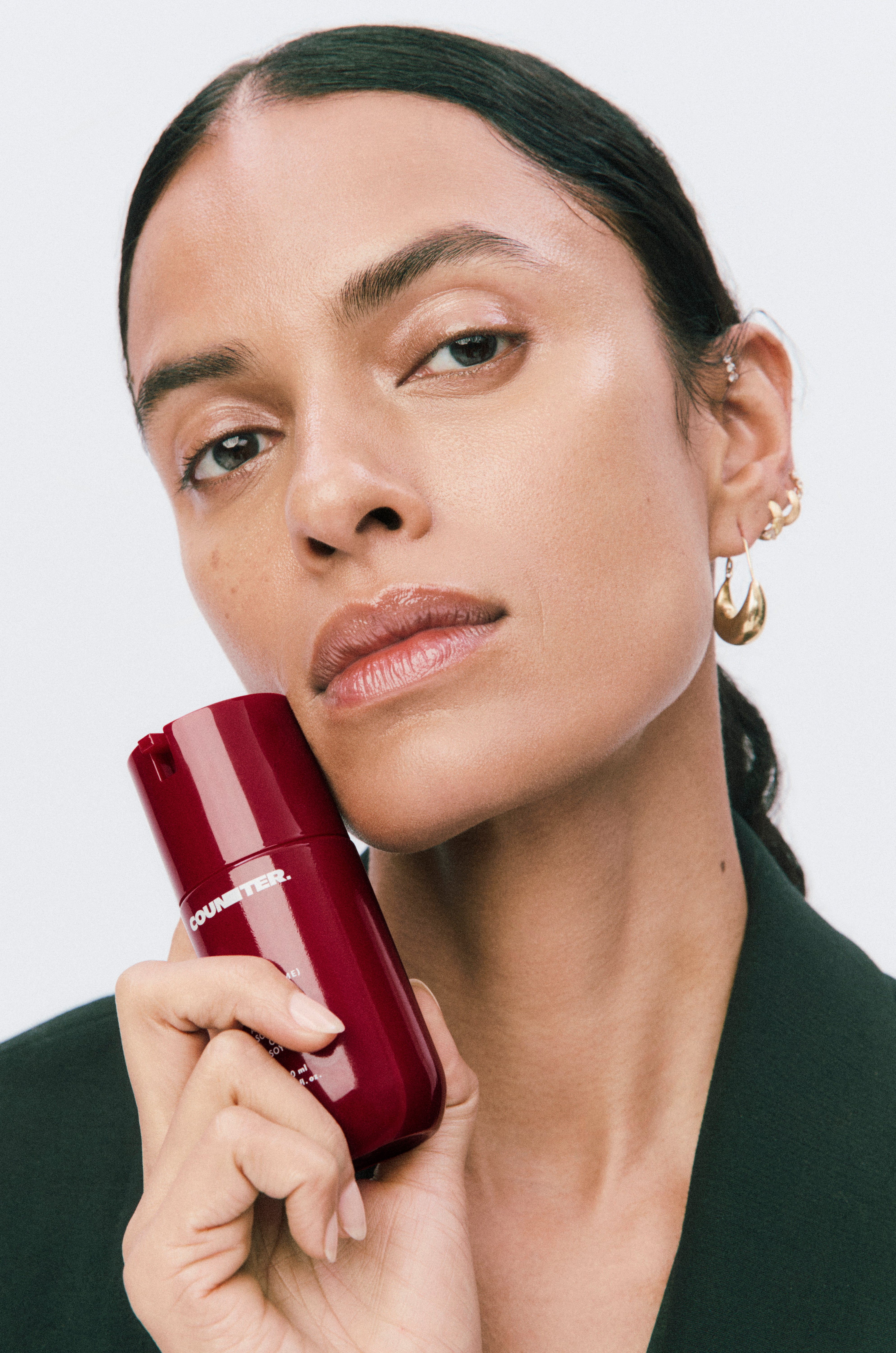 Displays a model holding a right red bottle of Counter product up to her cheek.