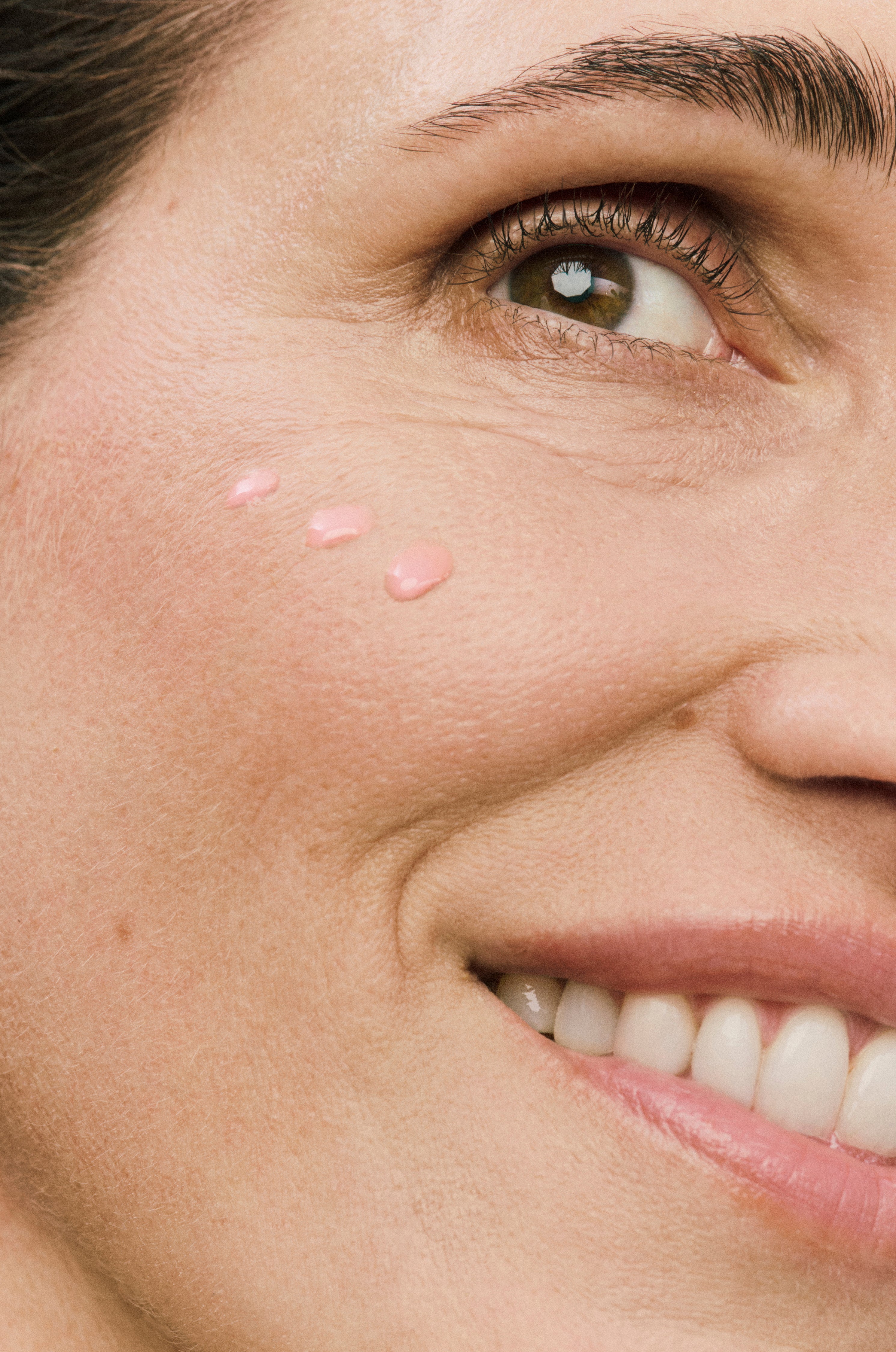 Displays a close up of a model's face with three dots of the pink countertime retinatural plus super serum on her cheekbone.
