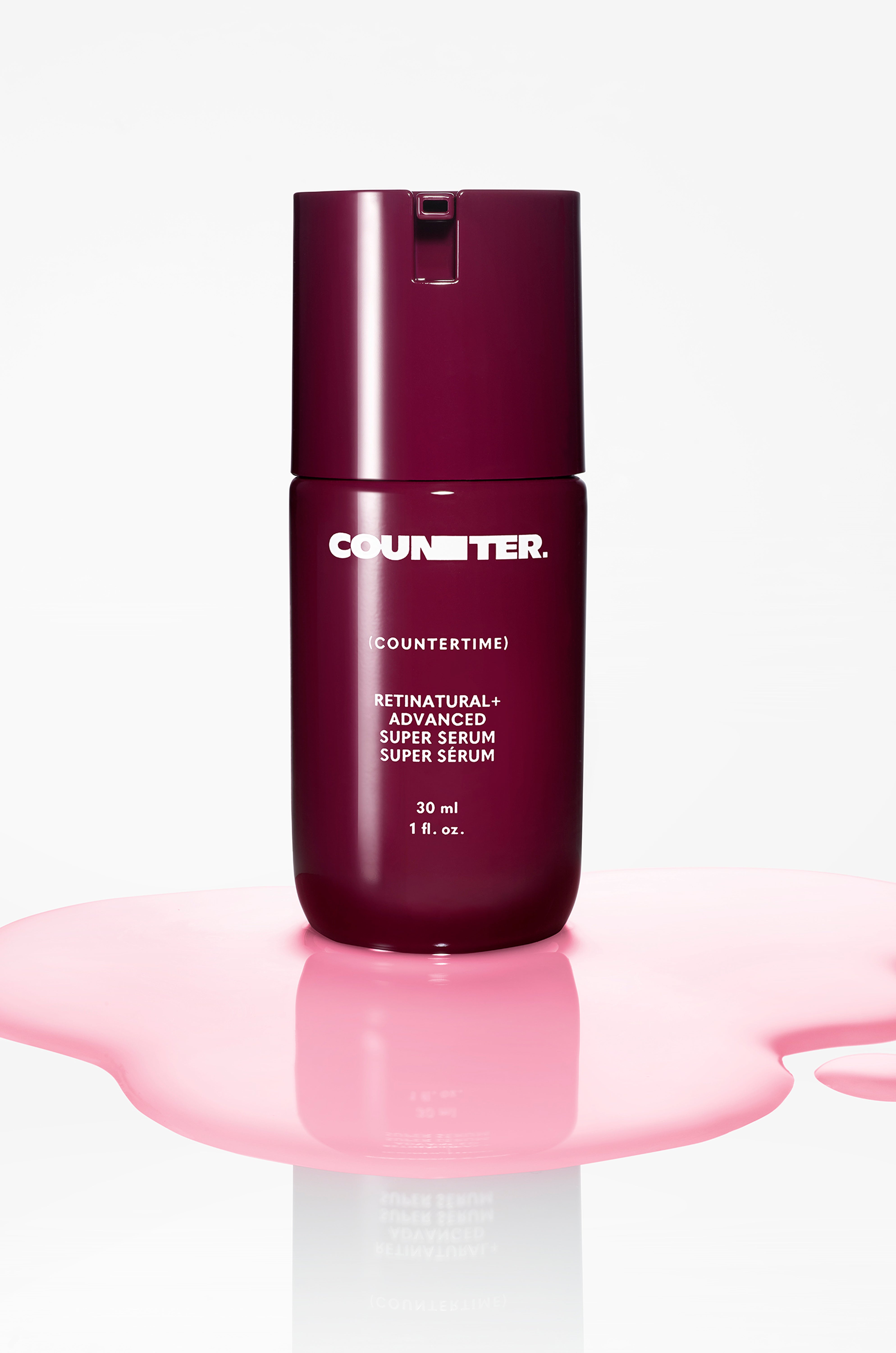 Displays the burgundy bottle of countertime retinatural + advanced super serum in a pool of the pink serum on a white background.