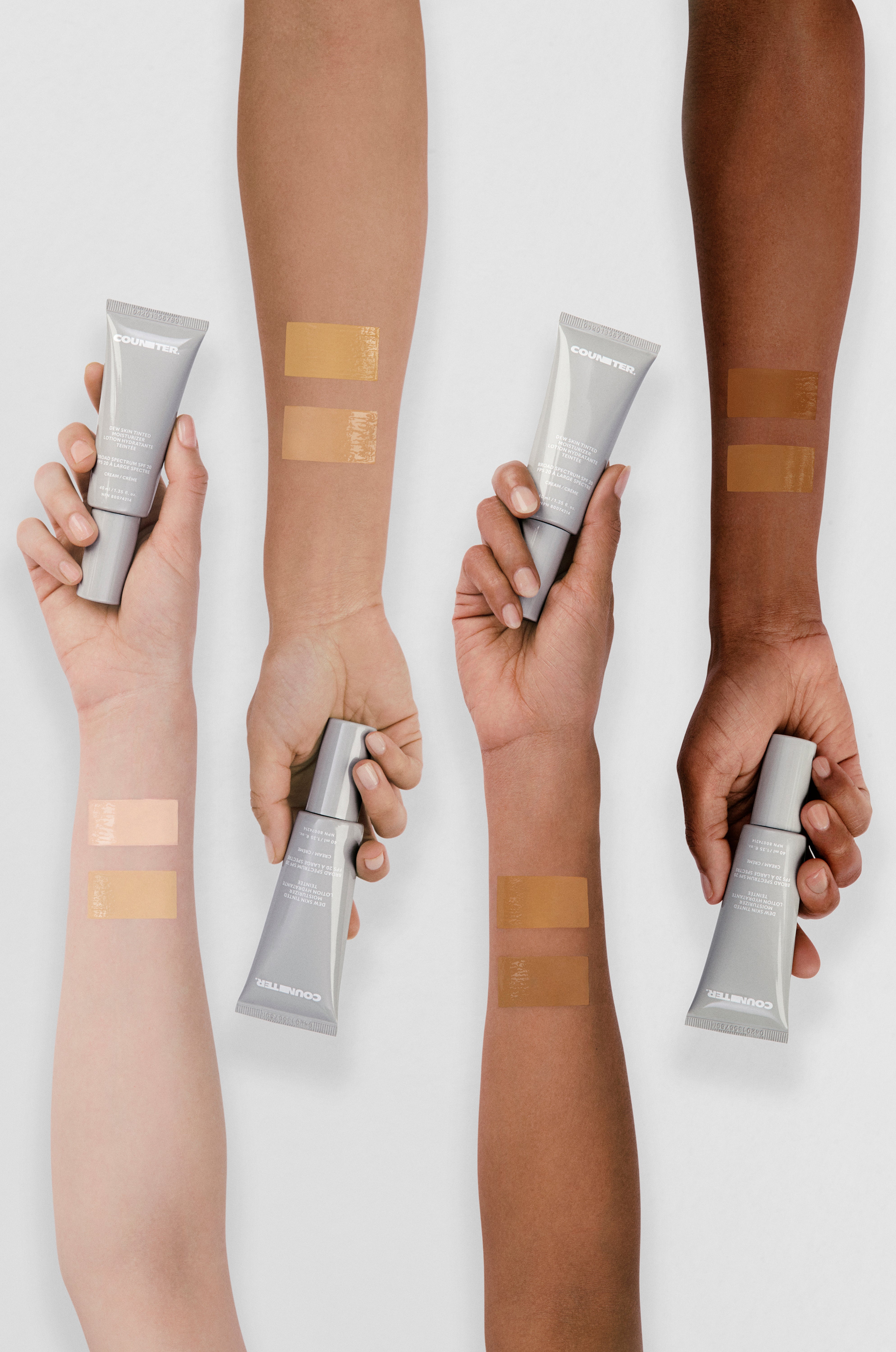 Hands holding cosmetic tubes with swatches on arms against a white background