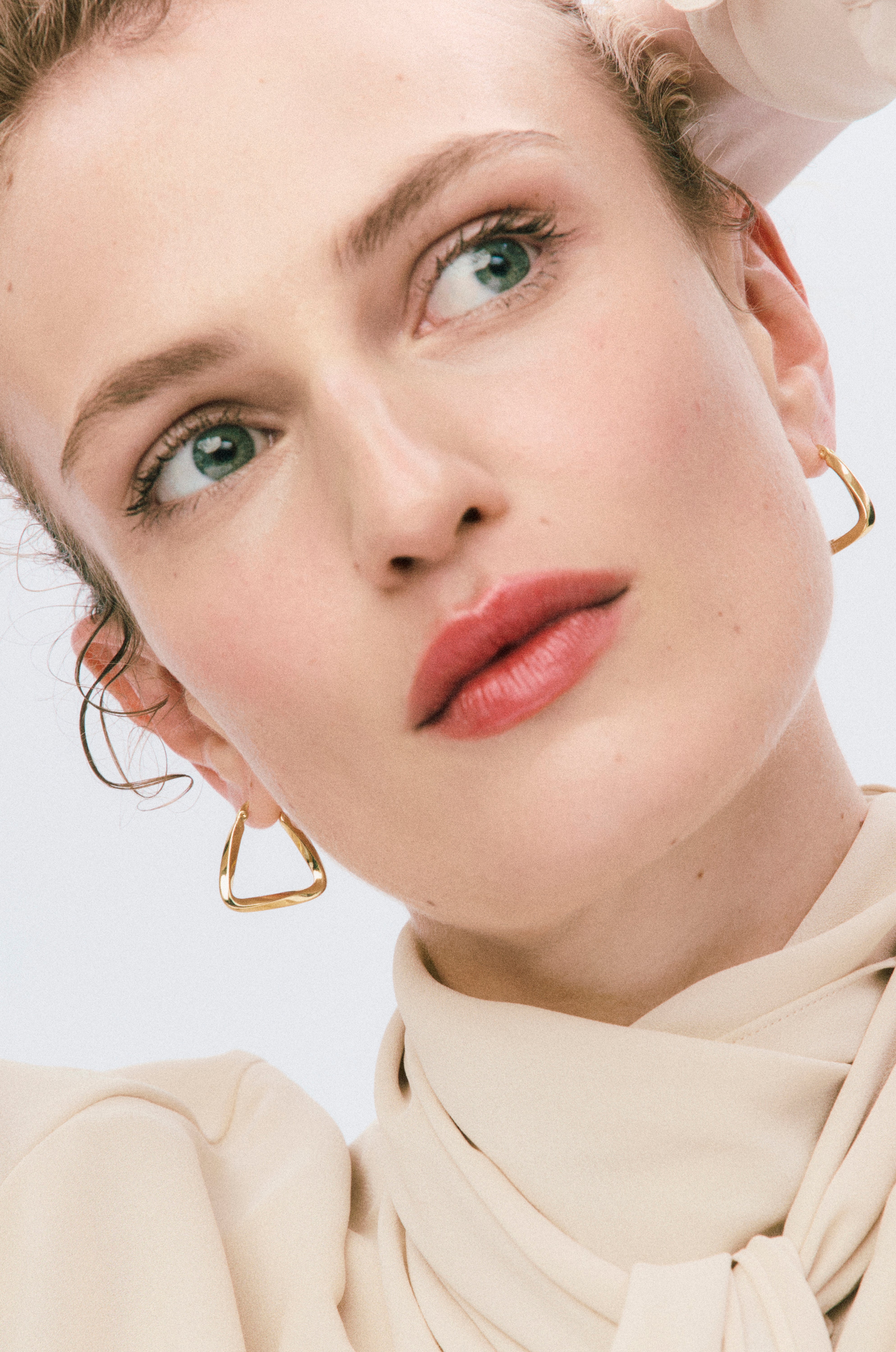 Close-up of a person wearing gold hoop earrings against a light background