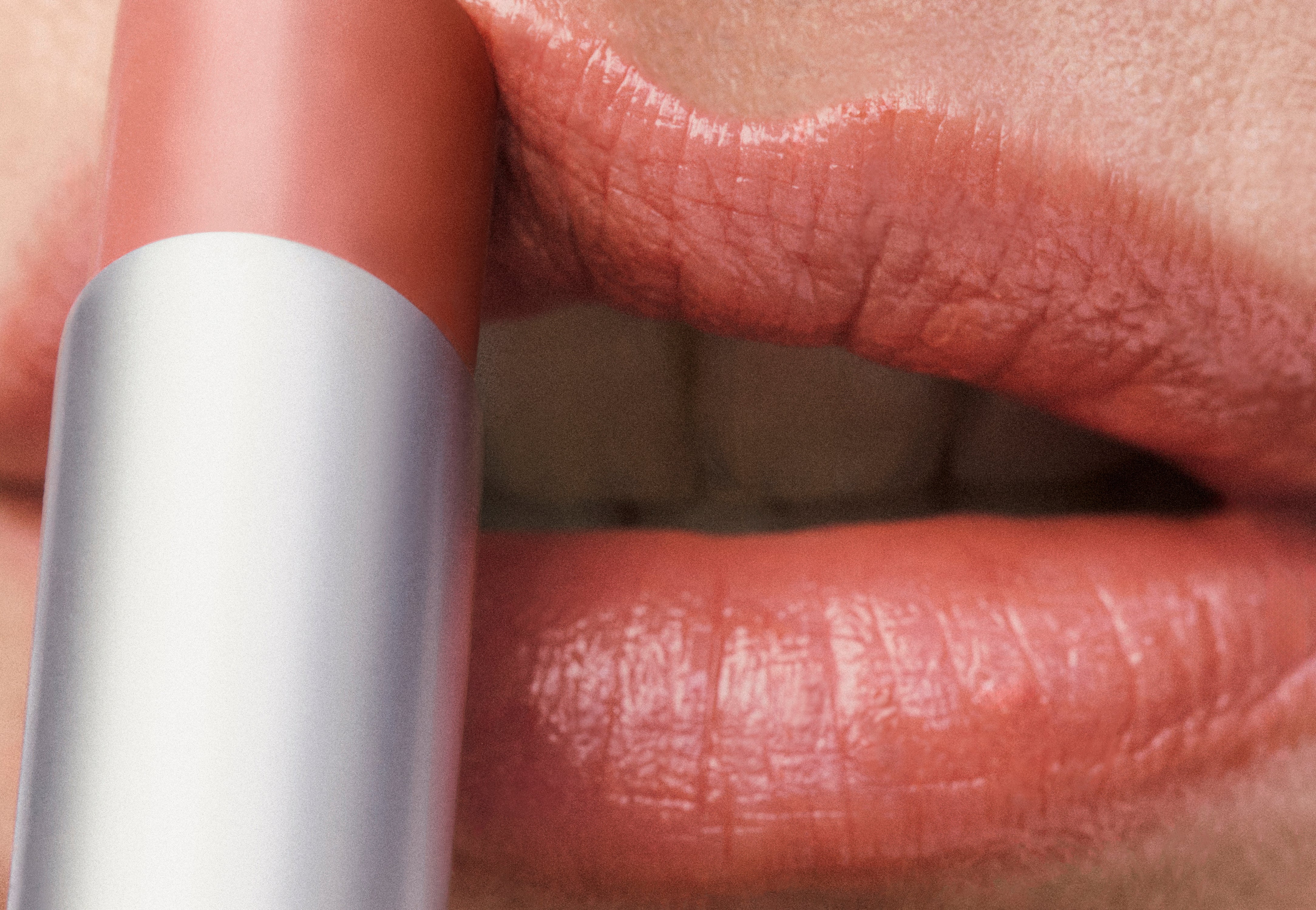 Displays a close up of a woman's lips with the Counter Sheer Genius conditioning lipstick in a peachy pink being applied.