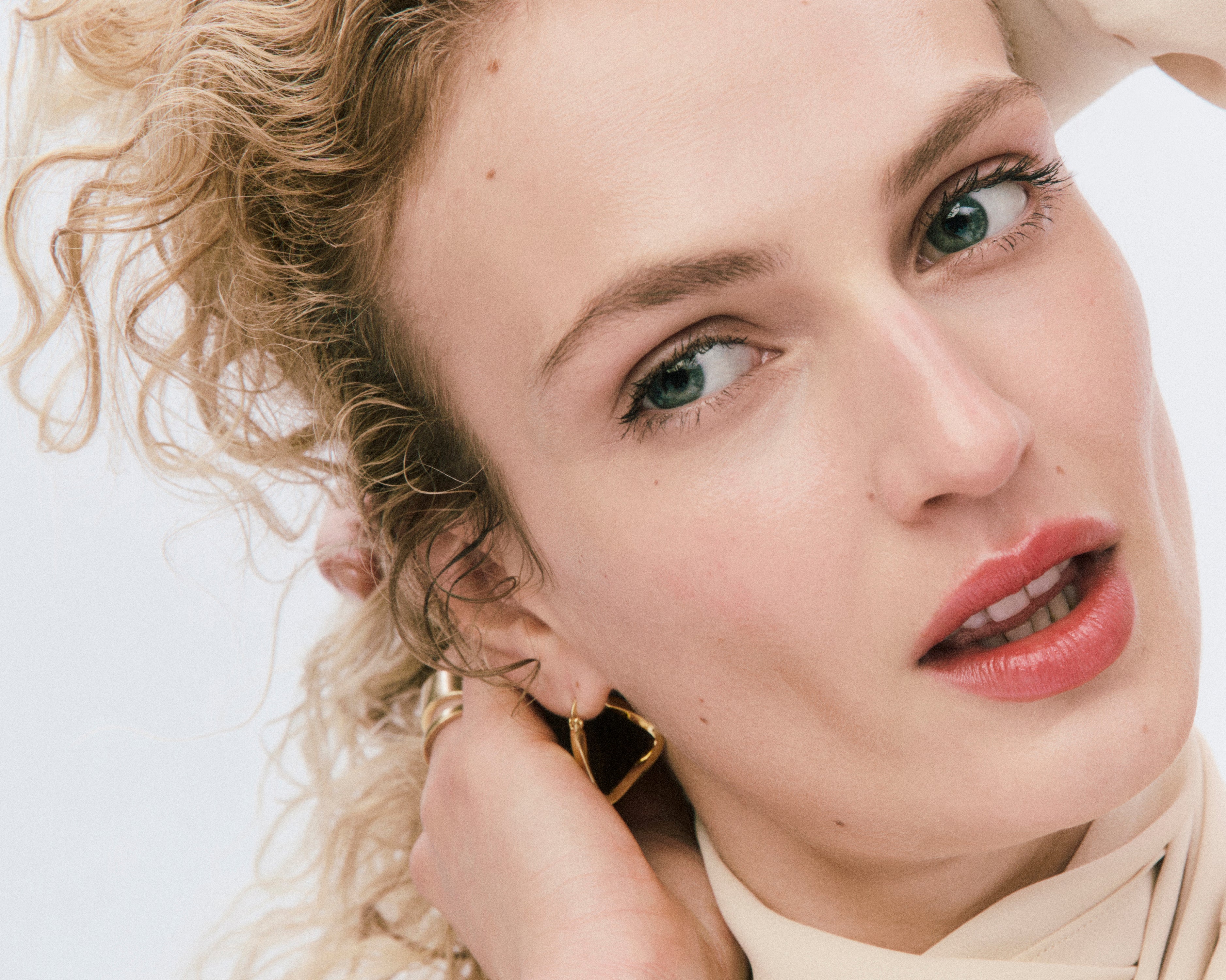 Displays a model with curly blonde hair and light eyes tilting her head towards the camera. She is wearing Counter products.