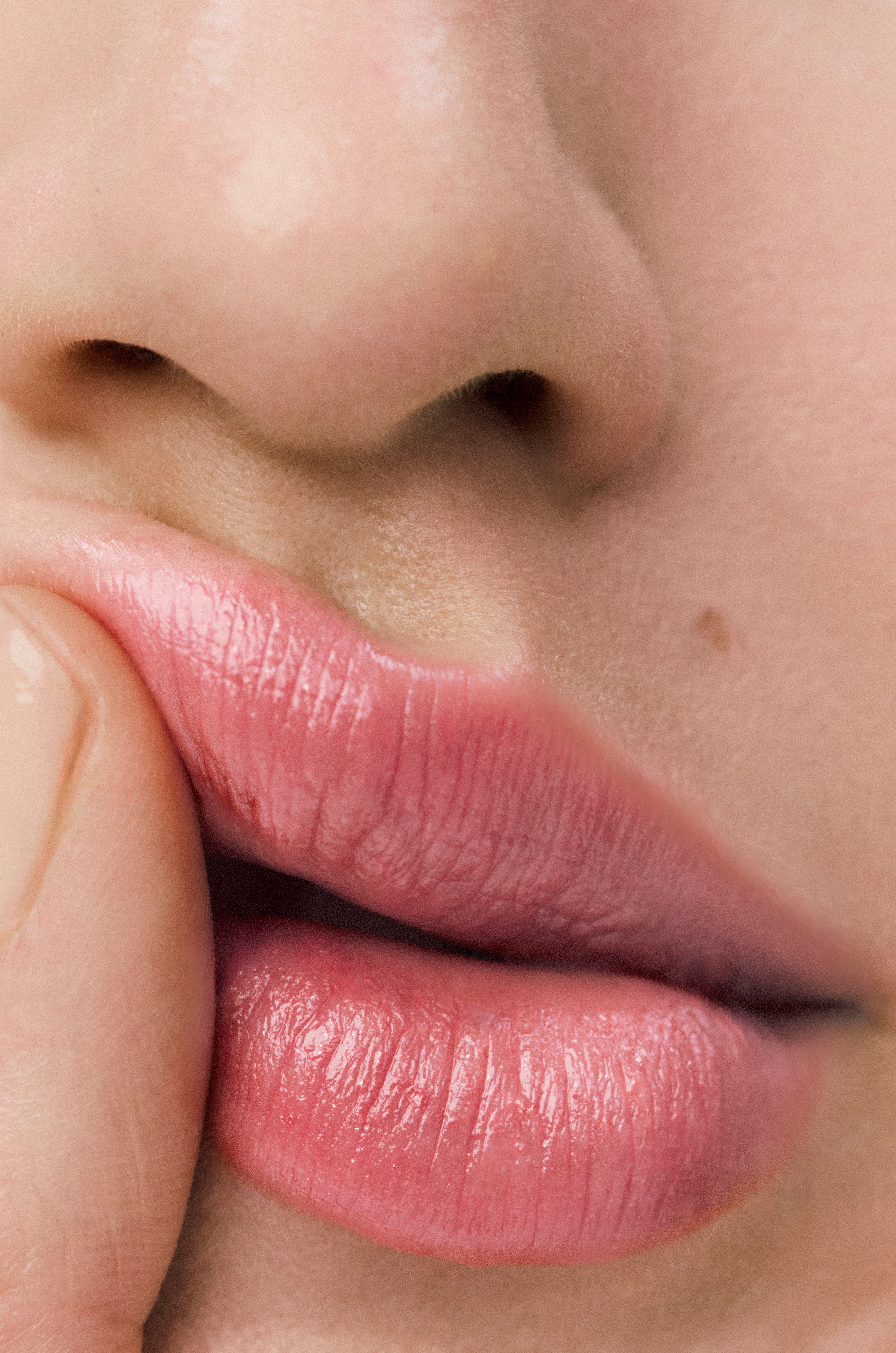 Displays a close up of a model's mouth where she is applying the Sheer Genius Conditioning Lipstick in Petal.