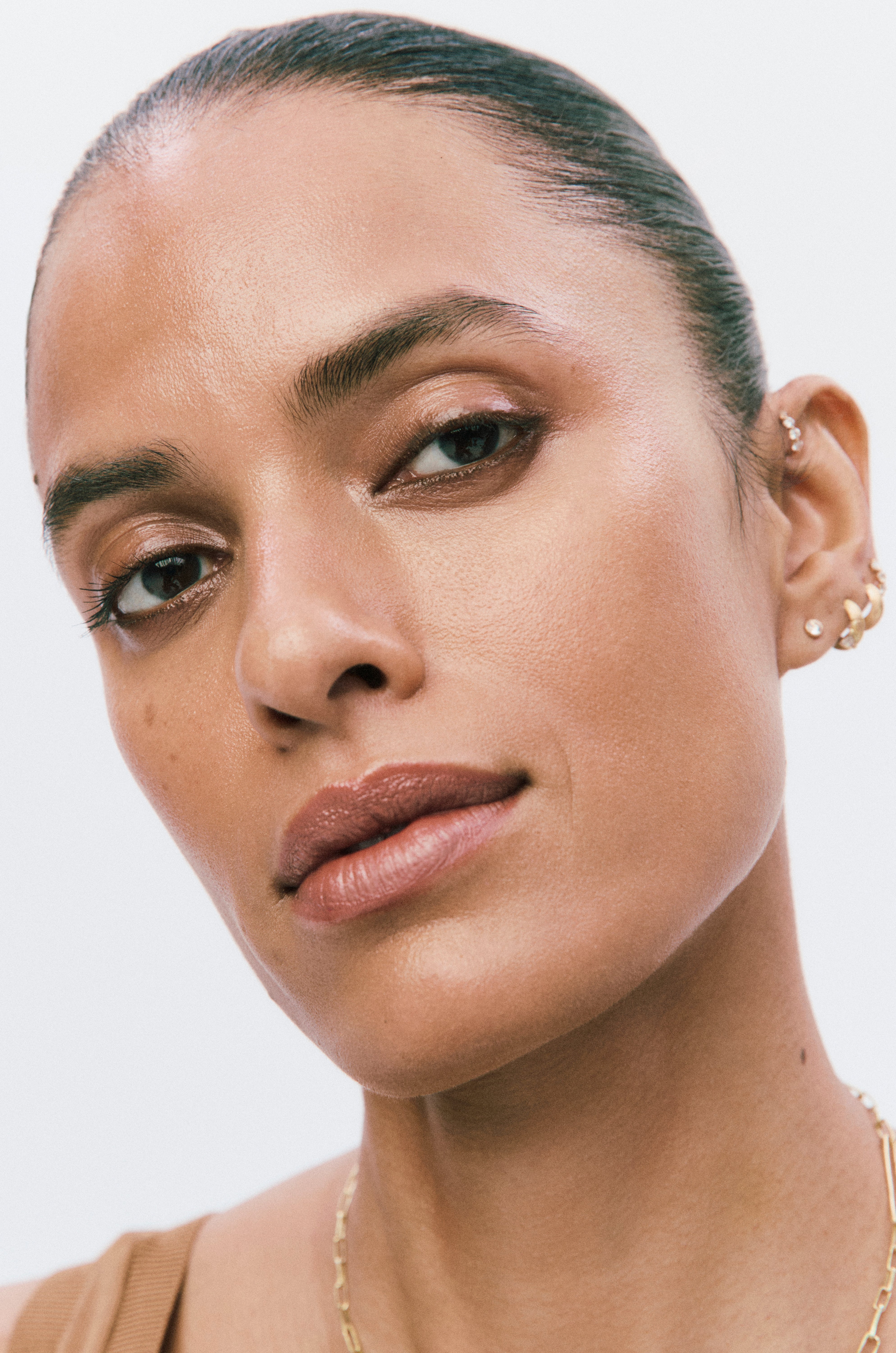 Close-up of a person wearing gold earrings and a necklace on a light background