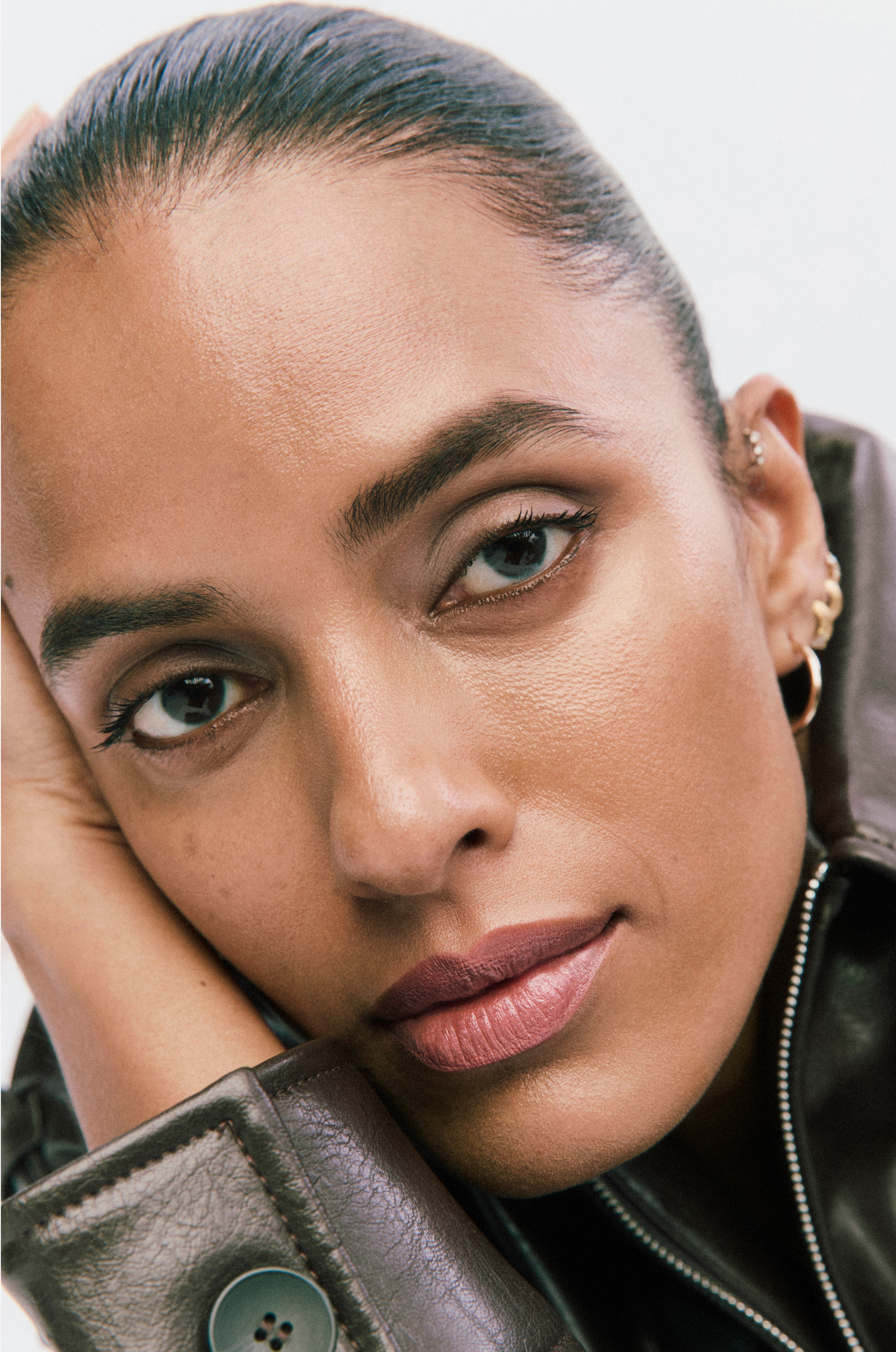 Displays a model in a leather jacket resting her face in her hand.