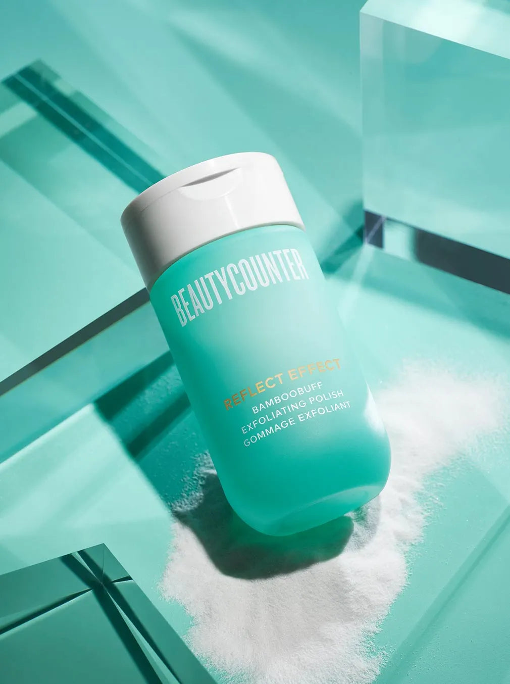 Displays the bright turquoise bottle and white lid of the Reflect Effect Bamboobuff Exfoliating Polish. The fine white powder is displayed underneath the bottle.