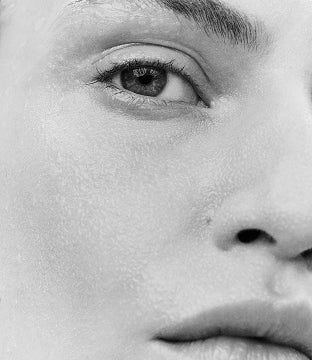 Displays a close up of half of a model's face in black and white.