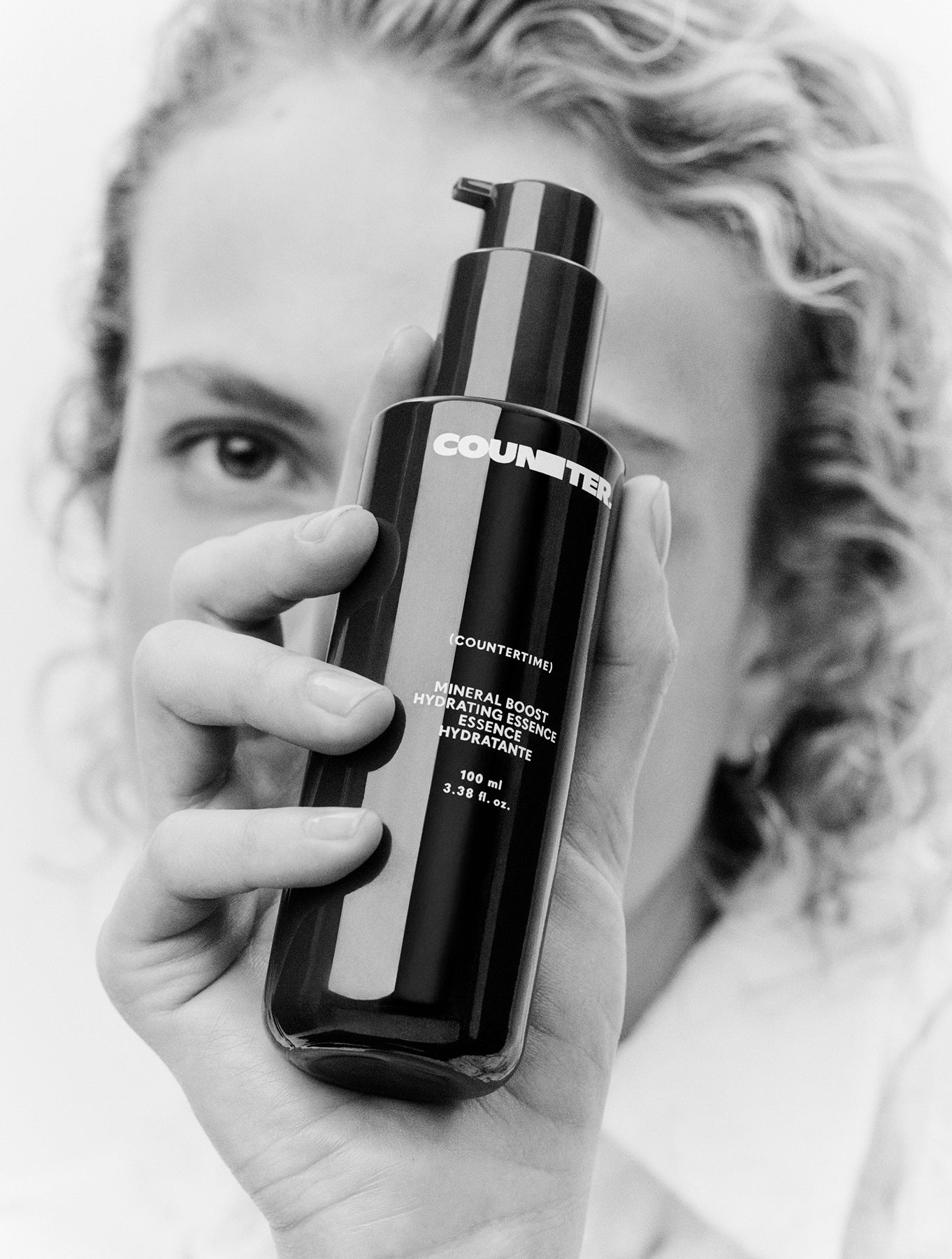 Displays a model holding a Countertime Mineral Boost Hydrating Essence in front of her face.
