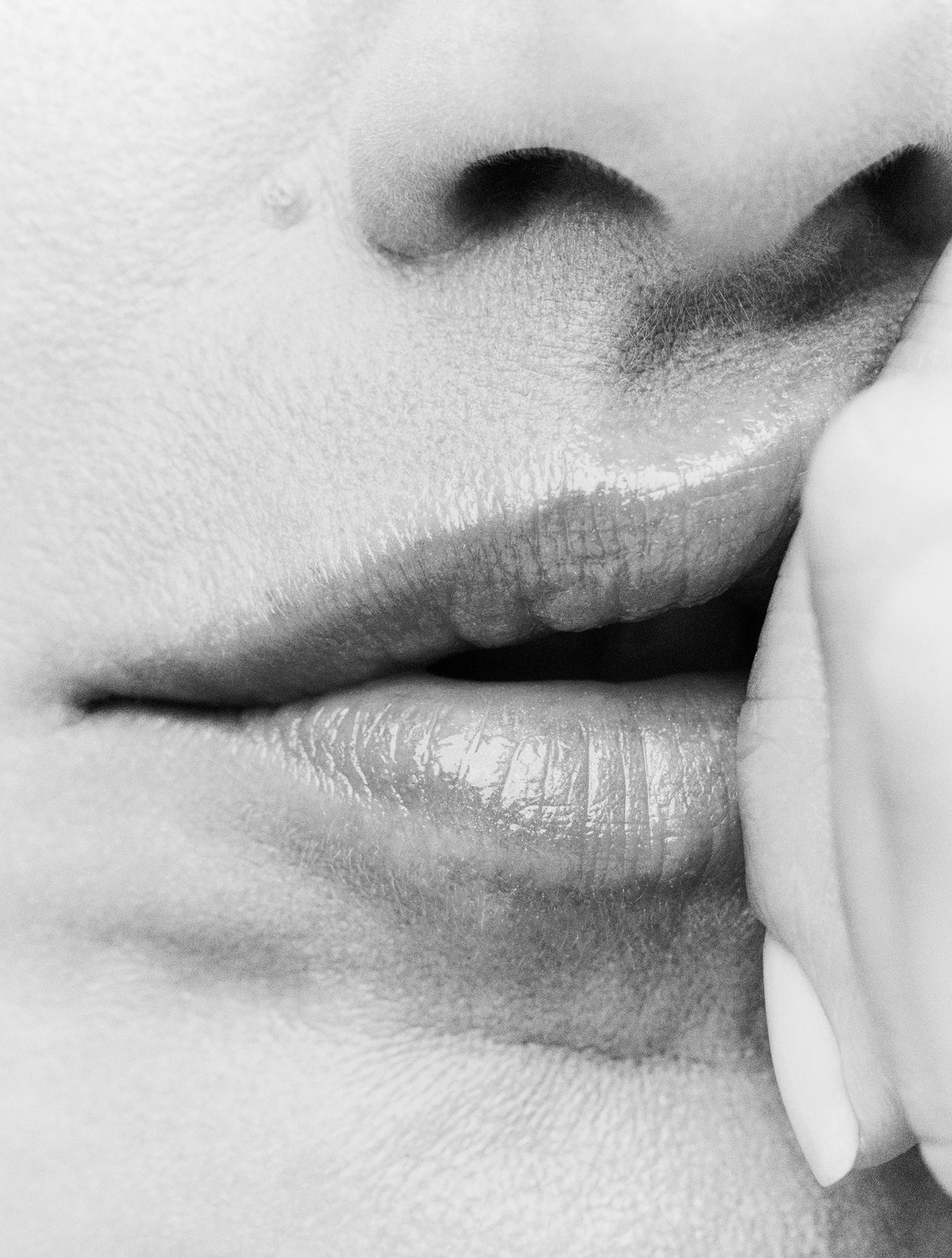 Displays a close of a model's mouth with her hand resting against her lips.