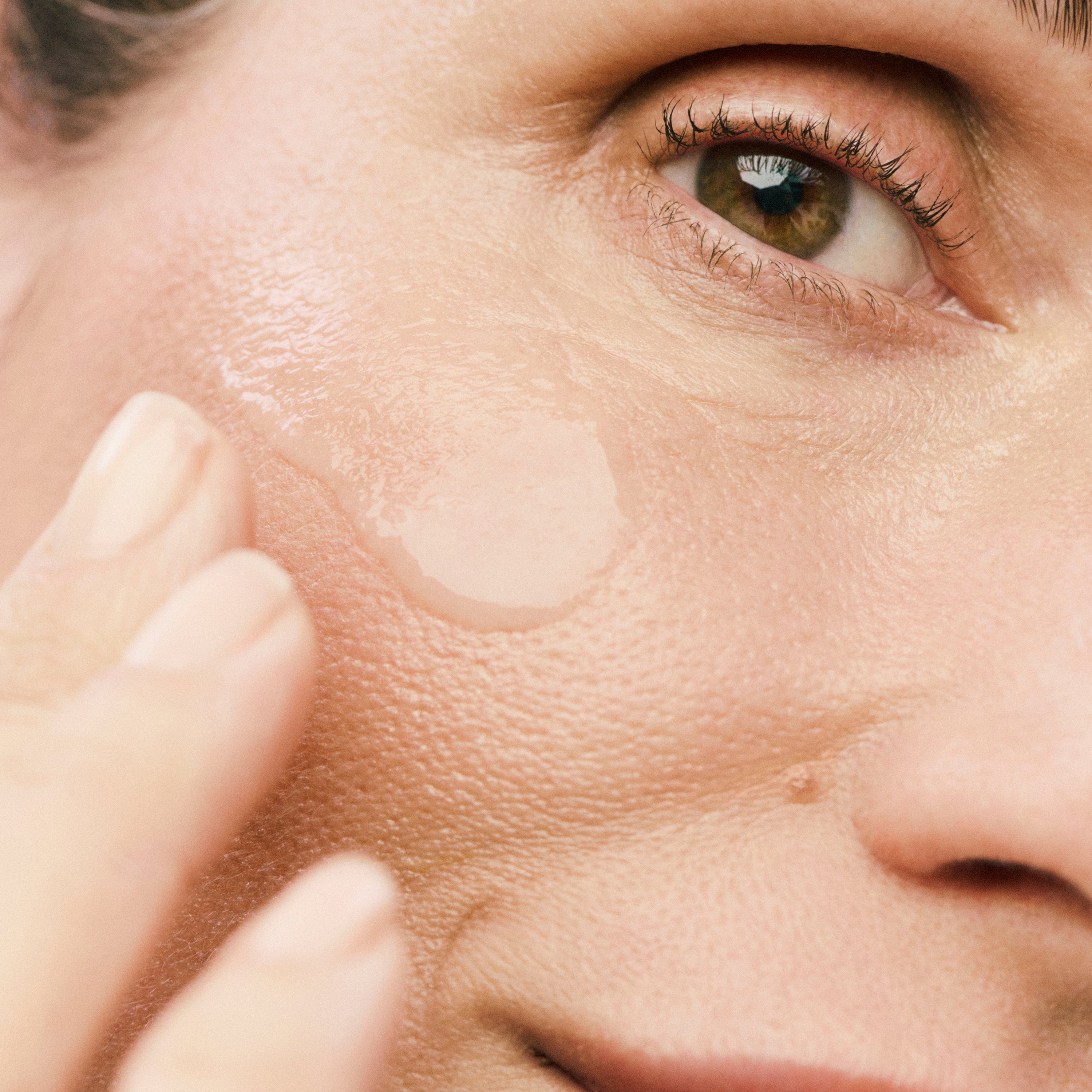 Displays a close up of a model's face with a clear smear of product on her cheekbone. 