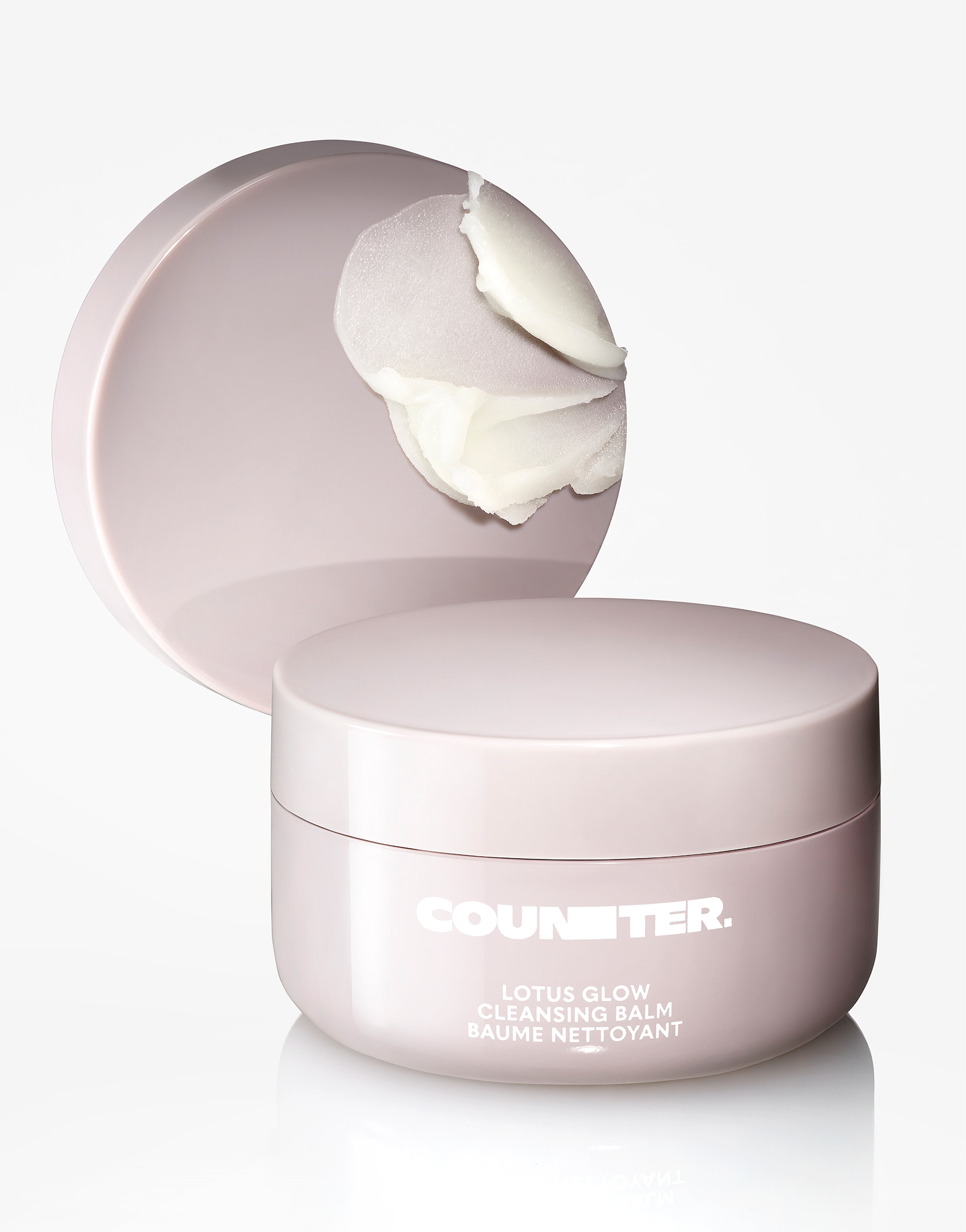 Displays a Counter Lotus Glow Cleansing Balm in a pale lavender jar with the product smear on a lid displayed behind the jar. 