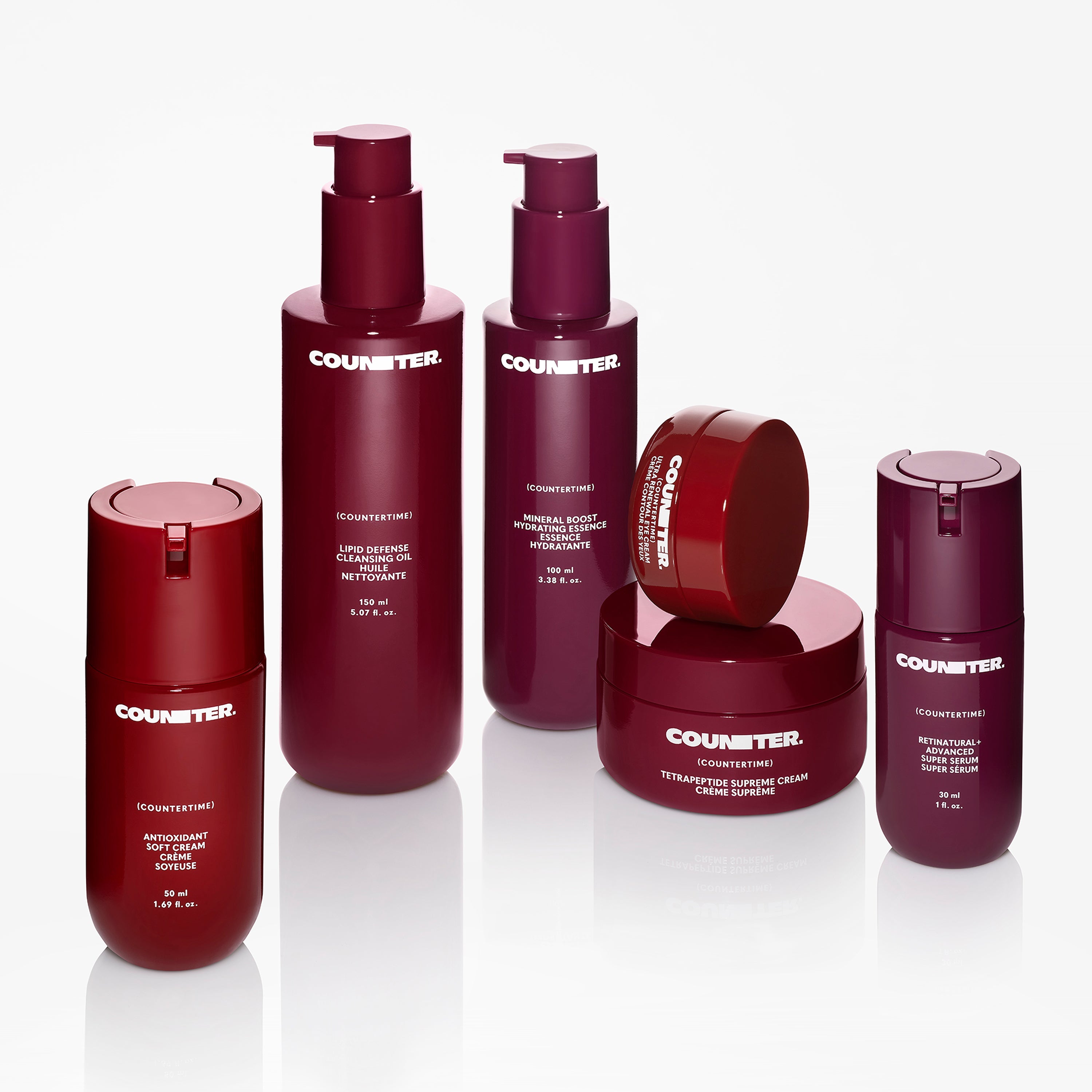 Displays products from the Counter Countertime line assorted on a mirrored surface. There are six products in varying shades of red and burgundy. 