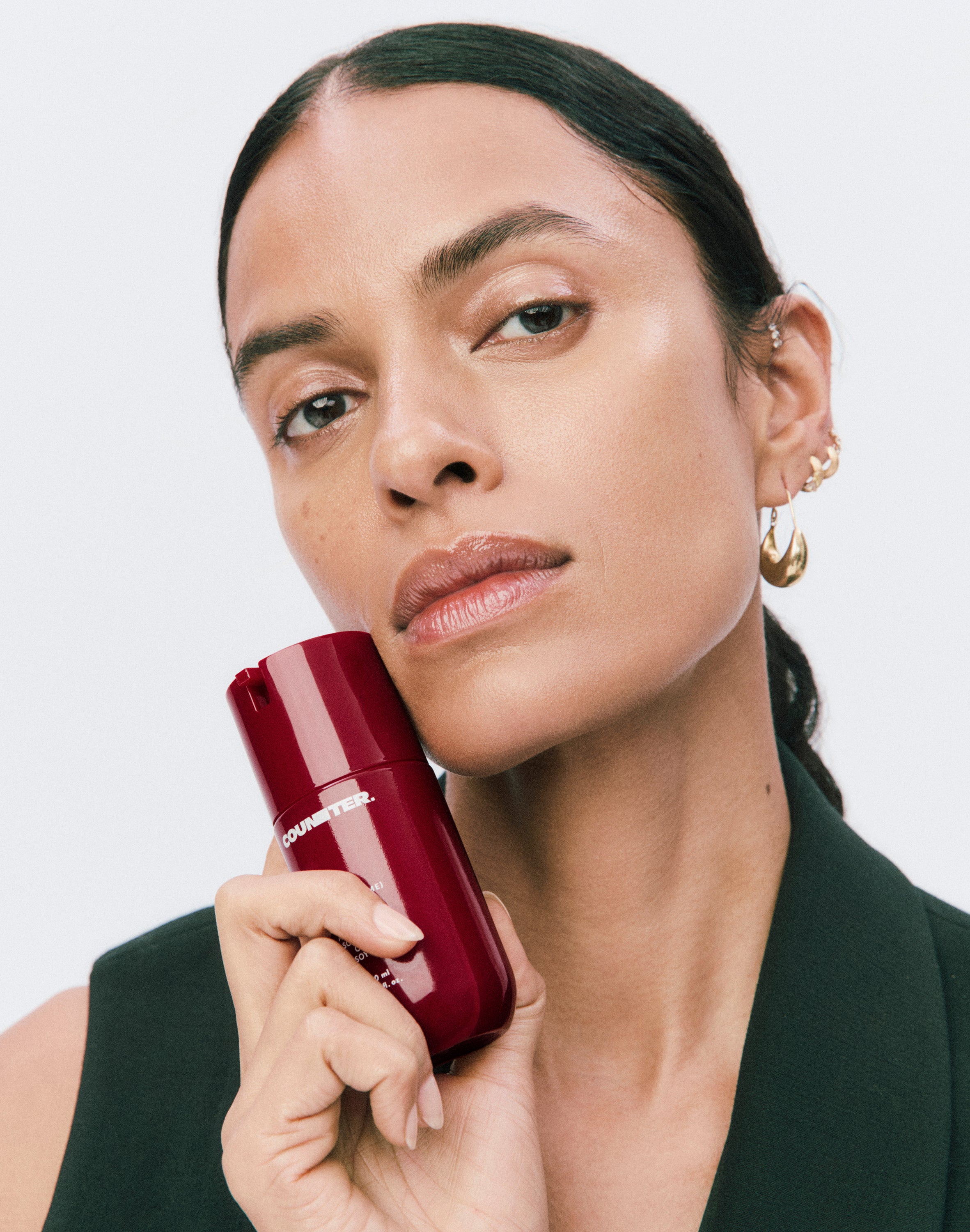 Displays a model holding a burgundy bottle of a Counter product up to her cheek. 